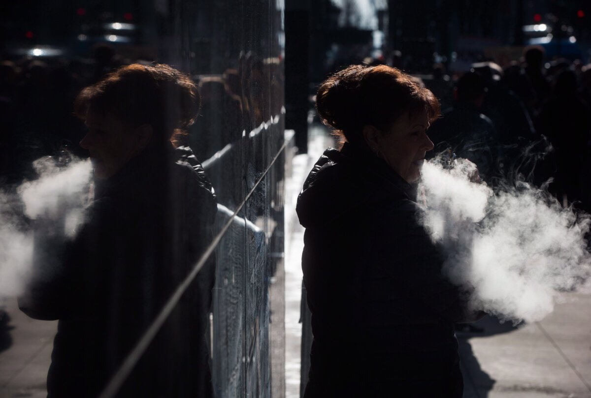 A woman exhales while smoking a vaporizer outside an office tower in downtown Vancouver on Feb. 28, 2017. (The Canadian Press/Darryl Dyck)