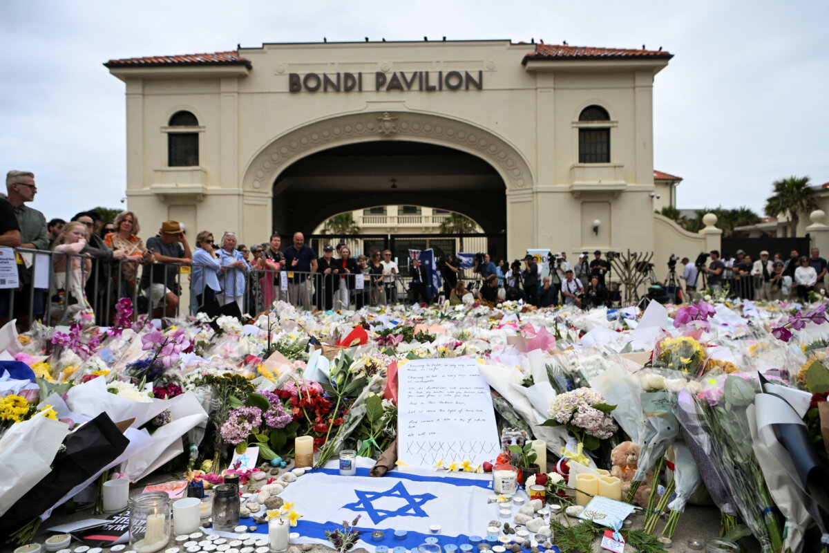 People stand near flowers laid as a tribute to honour the victims of a mass shooting that targeted a Hanukkah celebration at Bondi Beach in Sydney, Australia, on Dec. 16, 2025. (Flavio Brancaleone/Reuters)