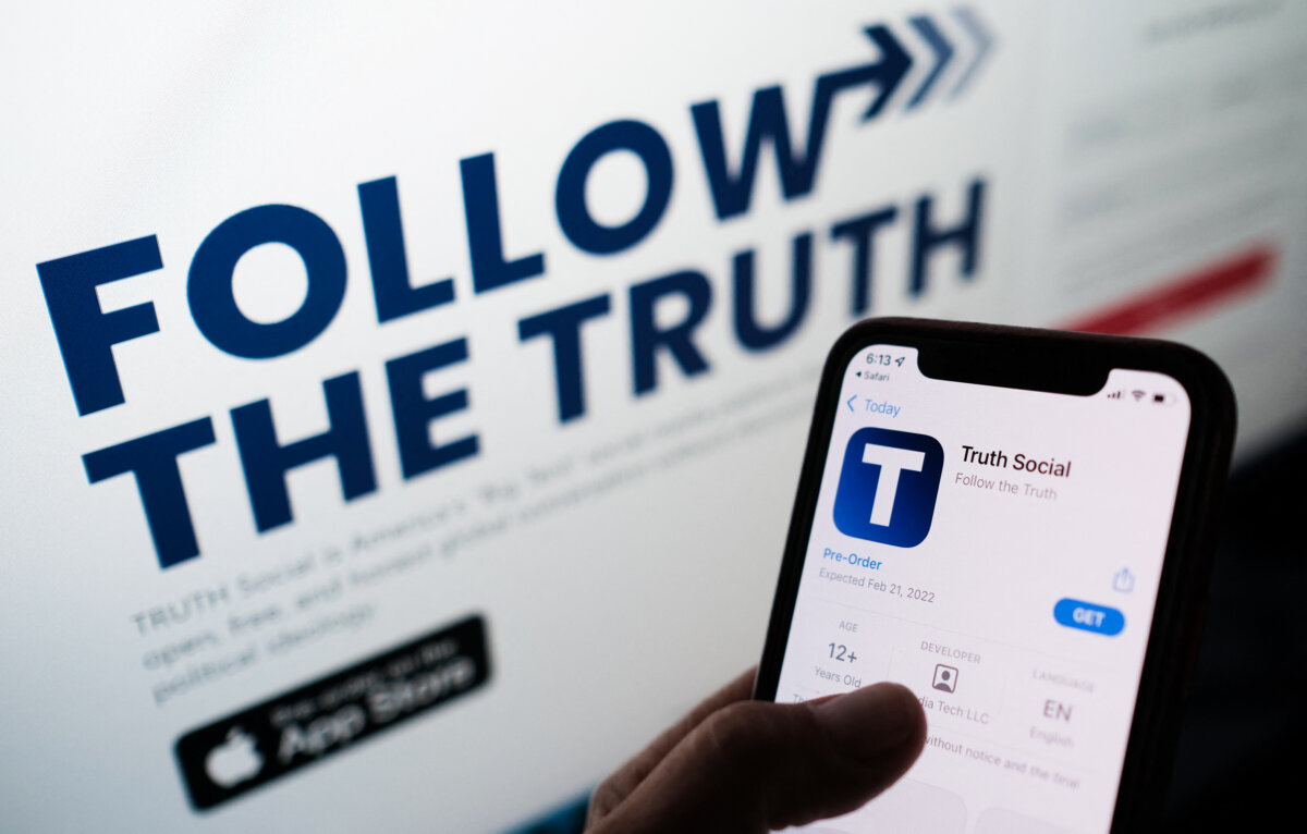 This illustration photo shows a person checking the app store on a smartphone for “Truth Social,” with it's website on a computer screen in the background, in Los Angeles, on Oct. 20, 2021. (Chris Delmas/AFP via Getty Images)