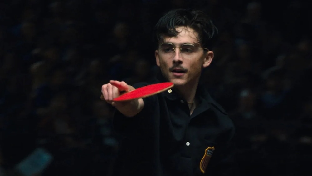 man with red ping pong paddle in Marty Supreme