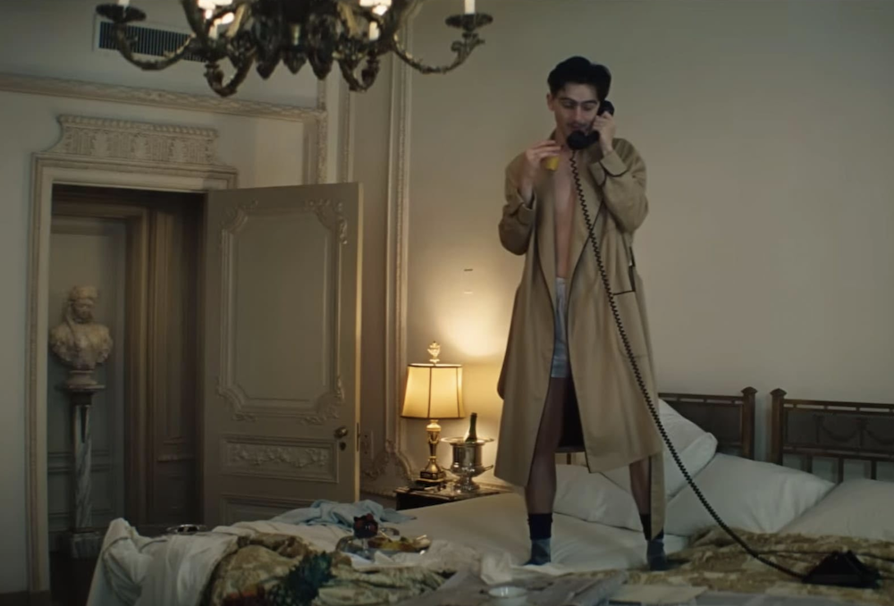 man on hotel bed on the phone in Marty Supreme