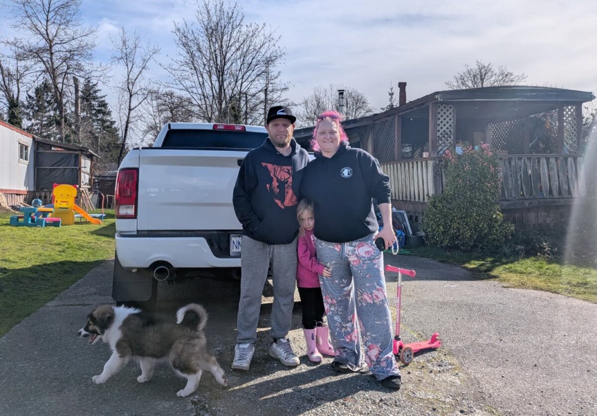William Hunt, his wife Kelsey Hunt, and their daughter stand outside their residence at the Queneesh Mobile Home Park in Comox, B.C., on March 9, 2026. Their dog Coda is in the foreground. (Paul Rowan Brian/The Epoch Times)