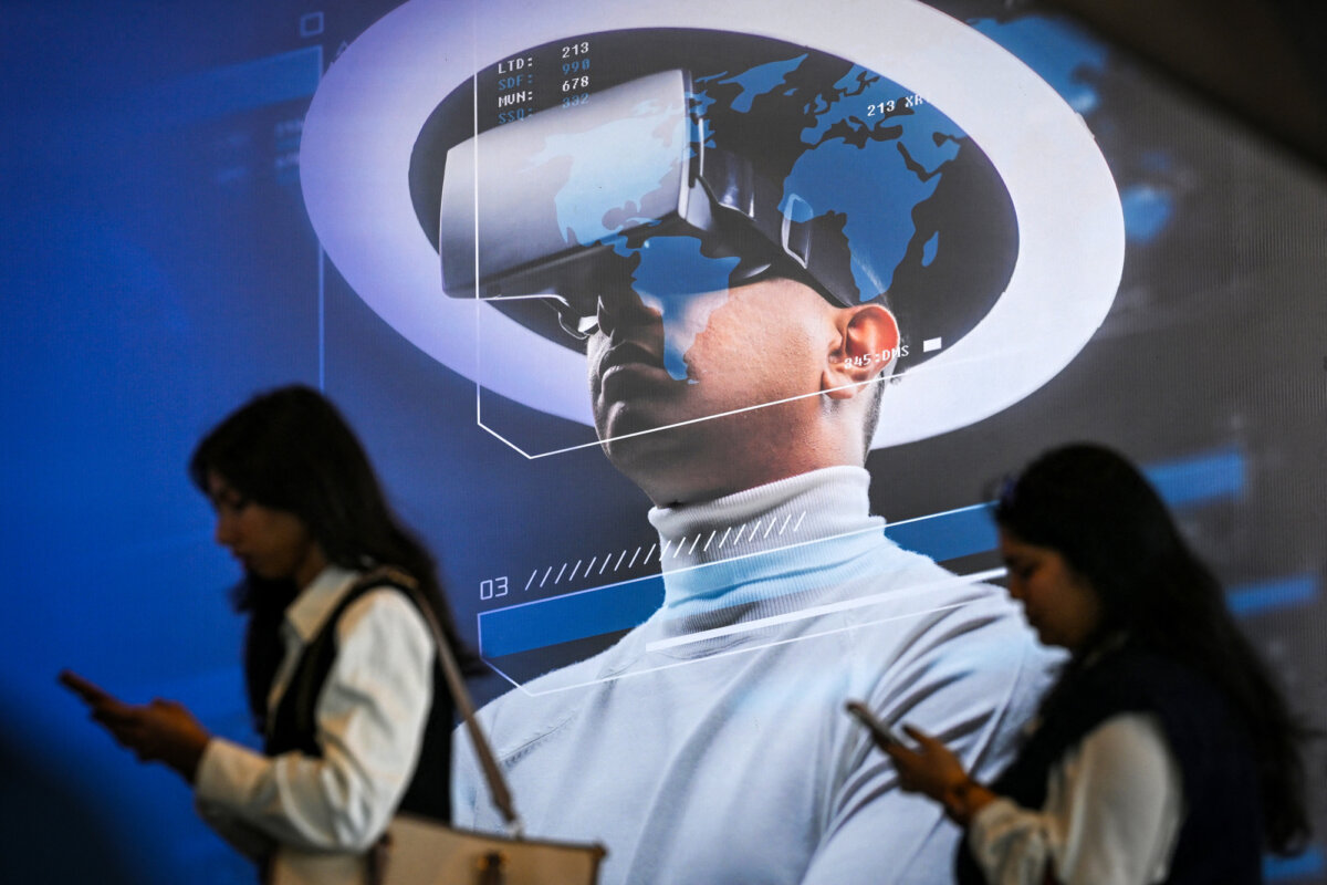 Visitors use mobile phones as they walk past a billboard advertising a virtual reality headset at the AI Impact Summit in New Delhi, India, on Feb. 17, 2026. A 2025 Anthropic report testing 16 large language models found all showed high-risk behavior in simulated environments. (Arun Sankar/AFP via Getty Images)