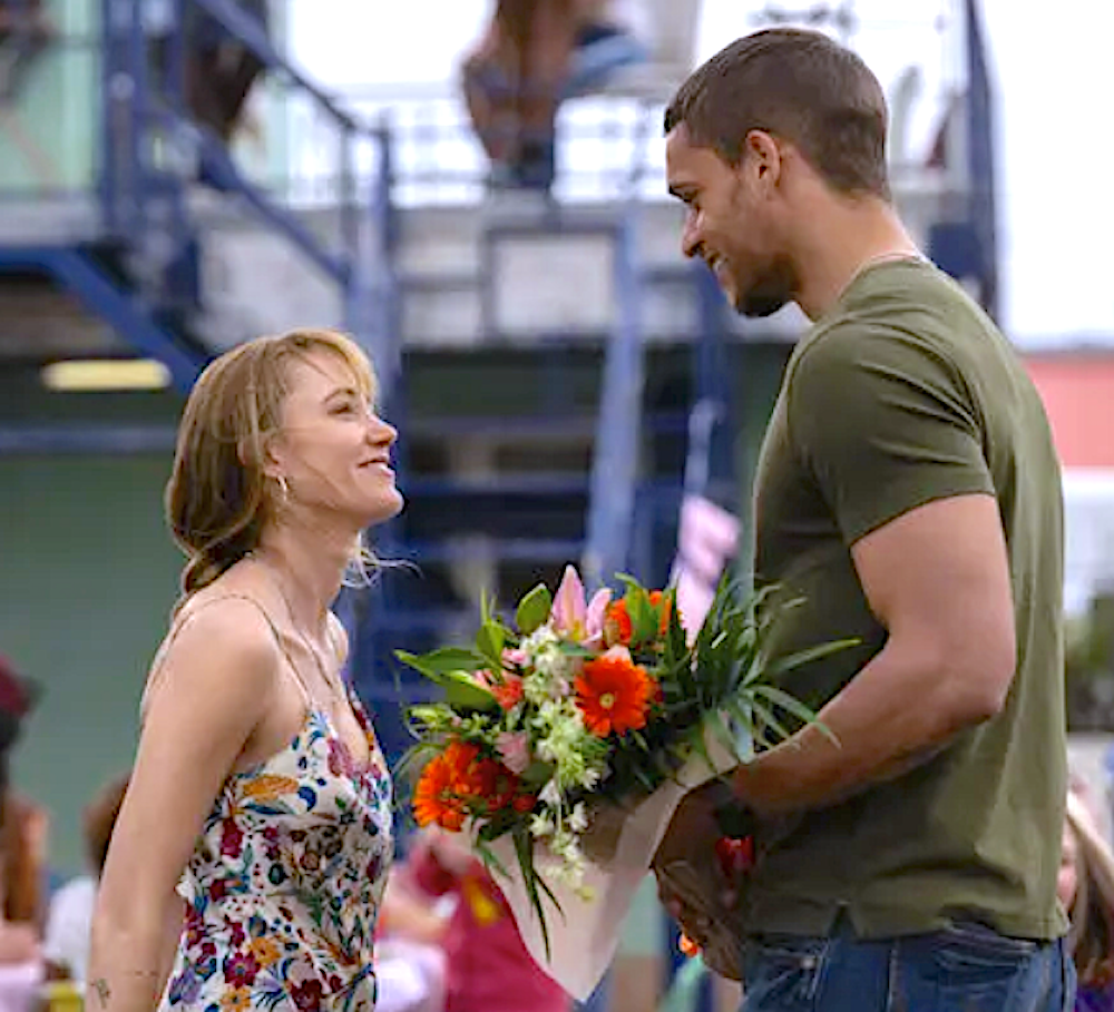 man in olive t-shirt brings blond woman flowers in Reminders of Him.