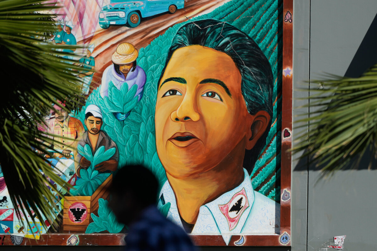A pedestrian walks below an image of Cesar Chavez on a mural in San Francisco on March 18, 2026. (AP Photo/Jeff Chiu)