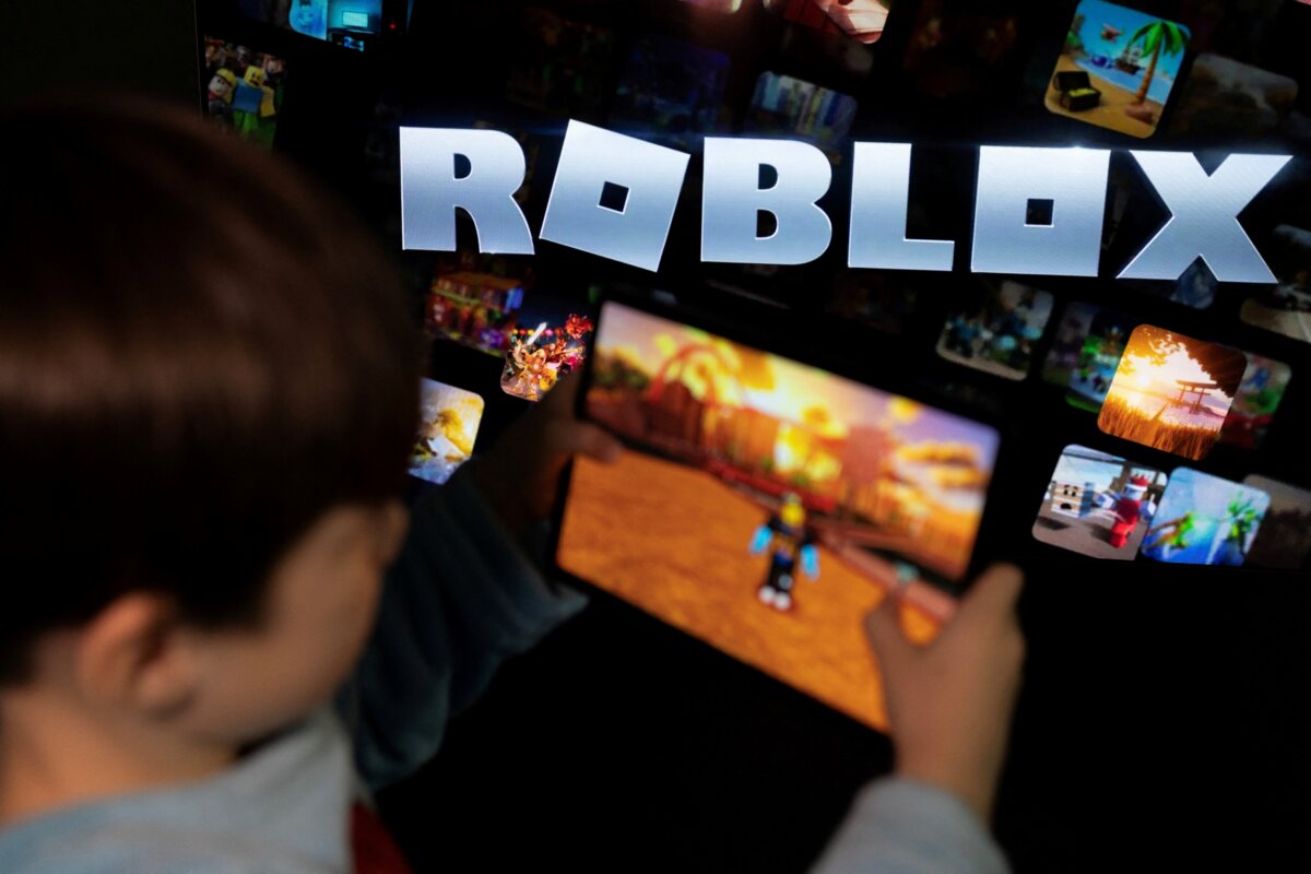 A boy poses for a photo while holding a game pad in front of a screen displaying the logo of the children's gaming platform Roblox, in this illustration taken on Dec. 8, 2025. (Ramil Sitdikov/Illustration/Reuters)
