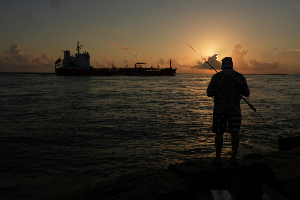 An oil tanker passes at sunrise while a man fishes in Port Aransas, Texas, on Aug. 9, 2025. (Eric Gay/AP Photo)