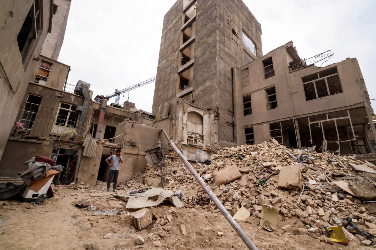 An Iranian man speaks on his mobile phone as he stands on the debris in front of destroyed buildings following a military strike on Tehran, Iran, on March 15, 2026. (Atta KENARE / AFP via Getty Images)