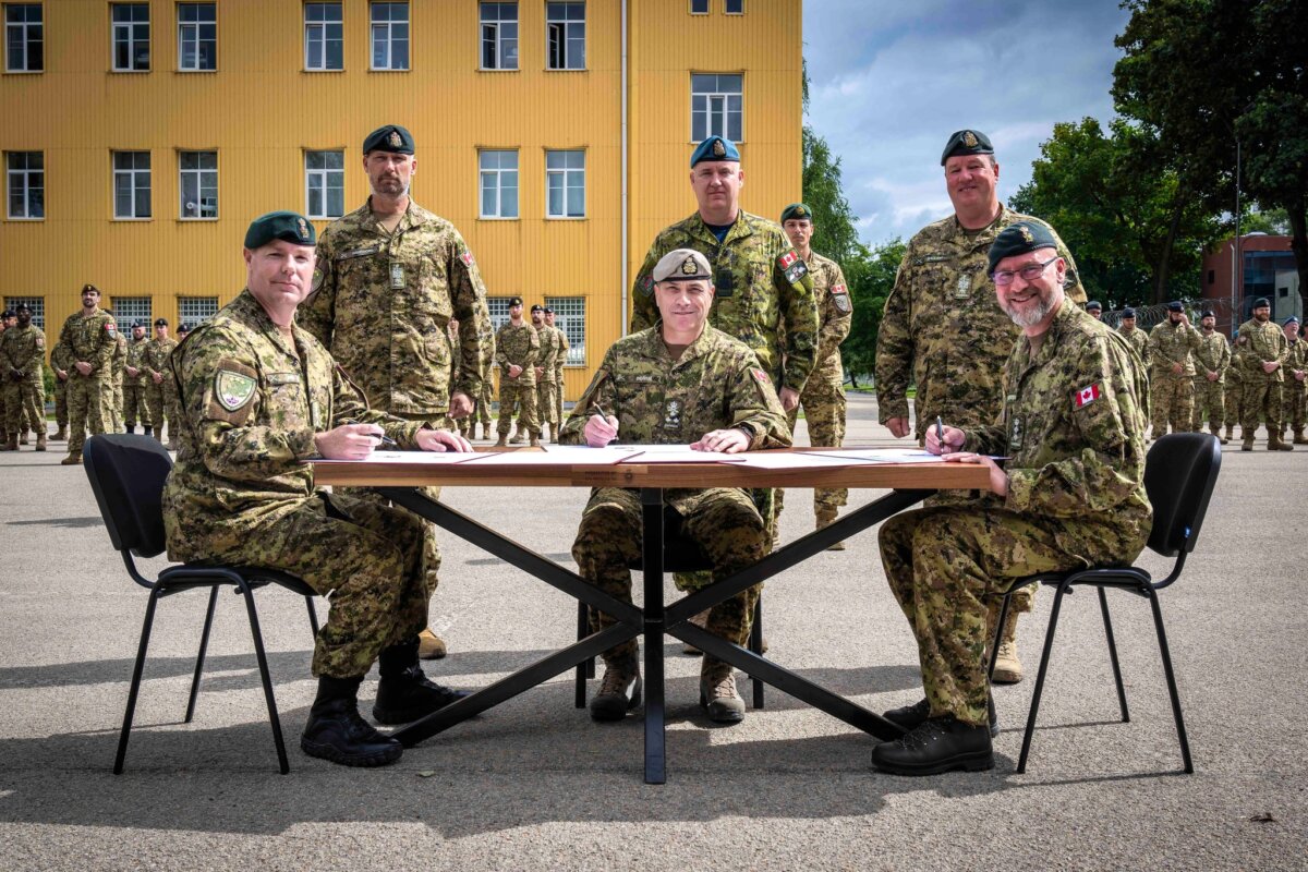 Lt.-Gen. Steve Boivin (seated centre) transfers command authority from Col. Vince Kirstein (seated right) to Col. James Smith (seated left) during parade for the Task Force Latvia change of command parade in Riga, Latvia on July 19, 2024. (Multinational Brigade Latvia Imagery-Canadian Imagery Technician RPBK)