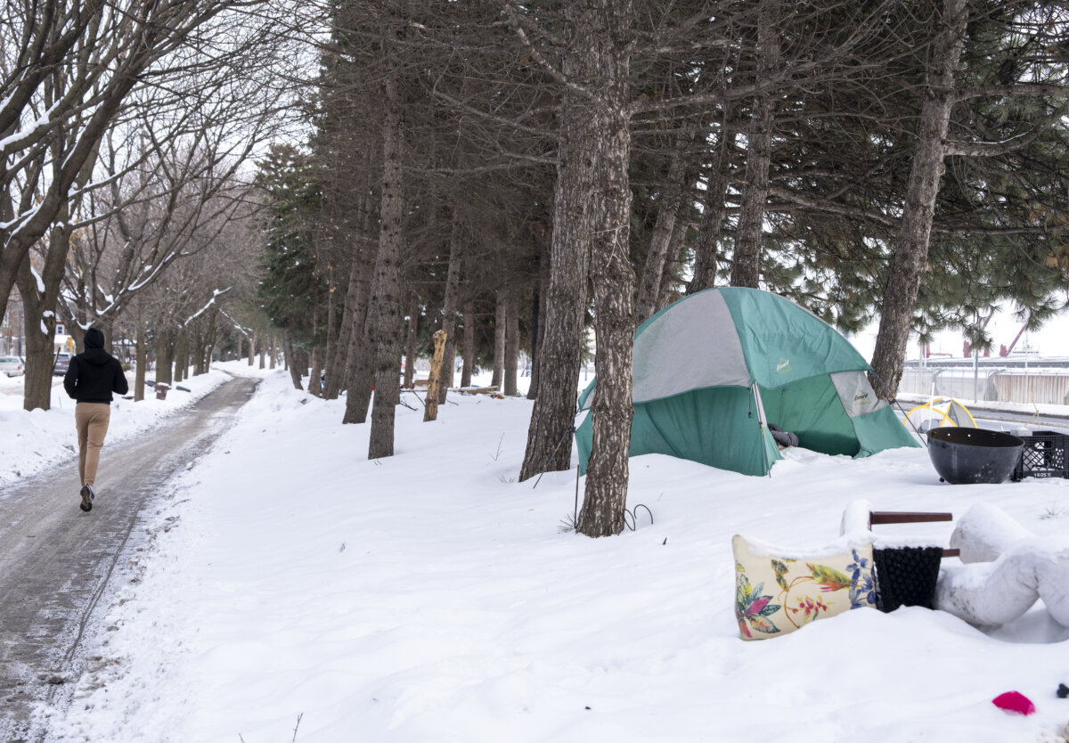A tent is seen at an unhoused encampment as a person jogs by in Montreal, on Feb. 27, 2026. (The Canadian Press/Christinne Muschi)