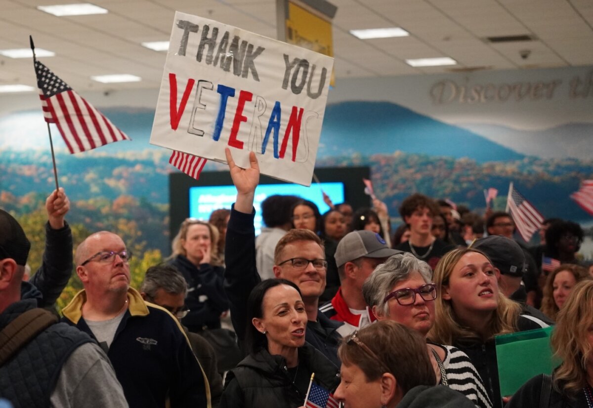 Orange County Legislator Jonathan Redeker holds a sign at Stewart International Airport in Newburgh, N.Y., on April 11, 2026. (Oliver Mantyk/The Epoch Times)