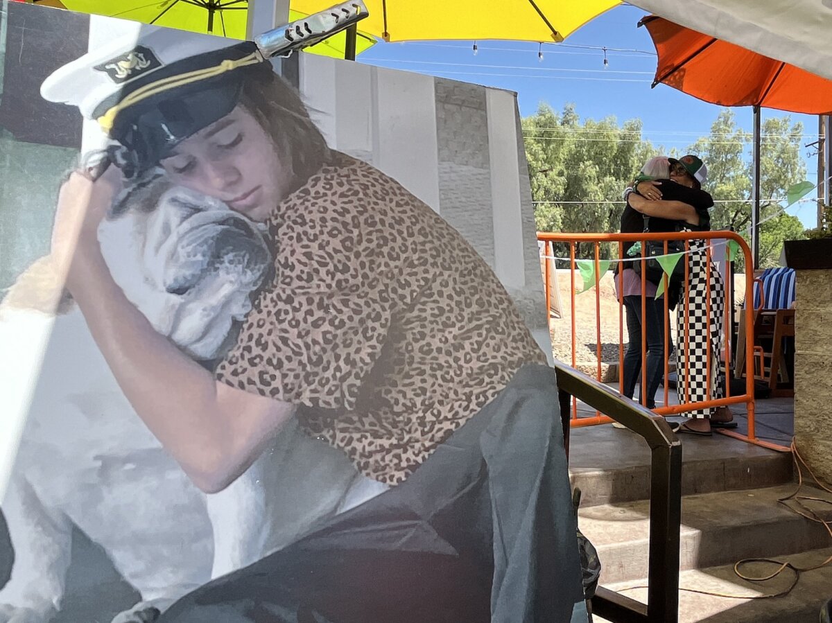 Megan Keller (R), mother of Cade Keller, greets a visitor with a hug during a yearly memorial fundraiser in Phoenix on April 18, 2026. In the foreground is her favorite photo of Caden, who died by suicide in March 2022. (Allan Stein/The Epoch Times)