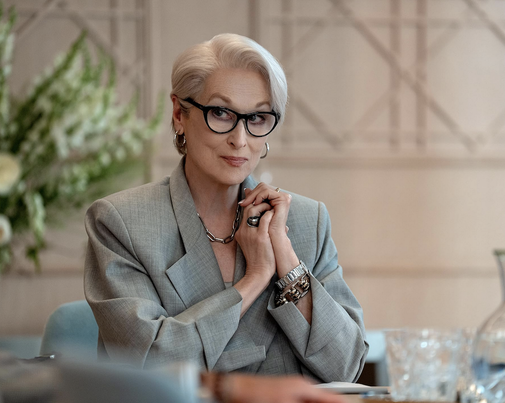 women wearing grey jacket sits at desk in The Devil Wear Prada 2