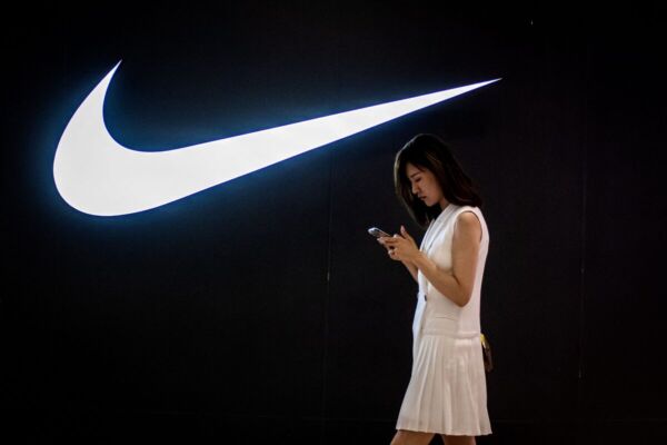 A woman browses her phone while walking past a Nike logo inside a shopping mall in Beijing on June 2, 2021. (Photo by Nicolas Asfouri/AFP via Getty Images)