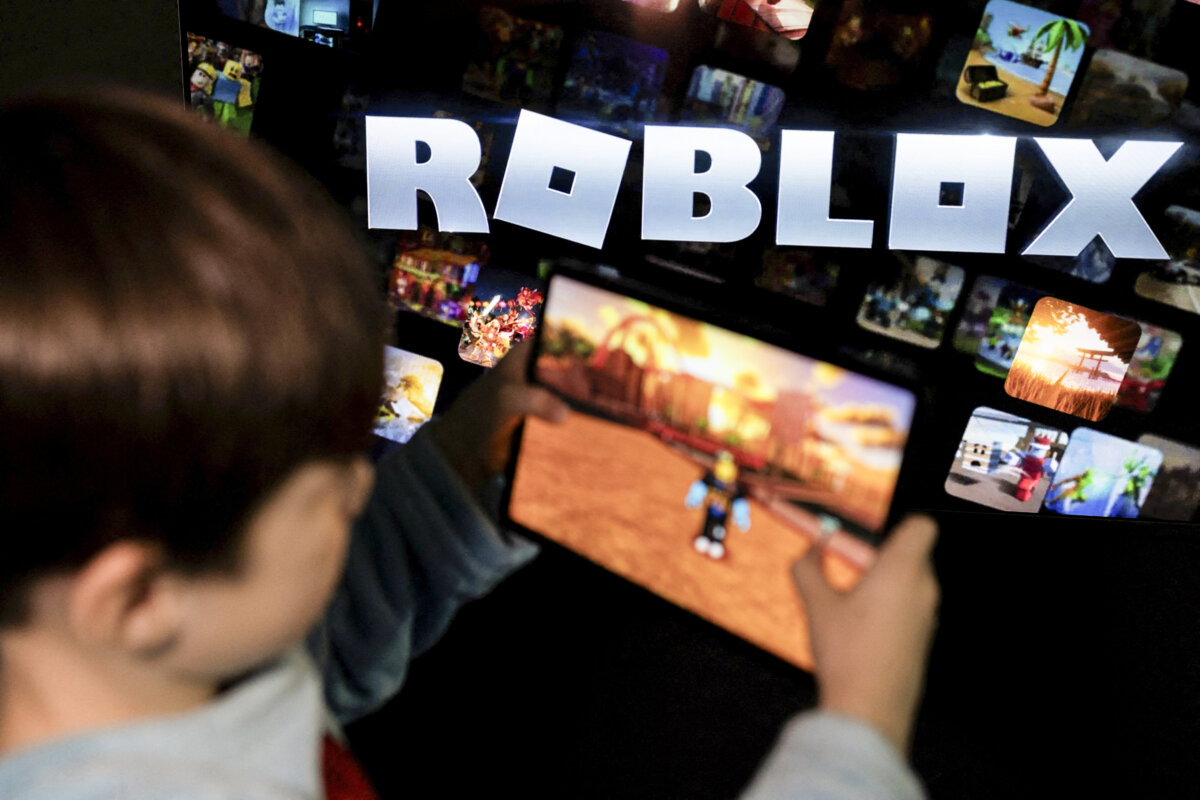 A boy poses for a photo while holding a game pad in front of a screen displaying the logo of the children's gaming platform Roblox, in this illustration taken on Dec. 8, 2025. (Ramil Sitdikov/Illustration/Reuters)