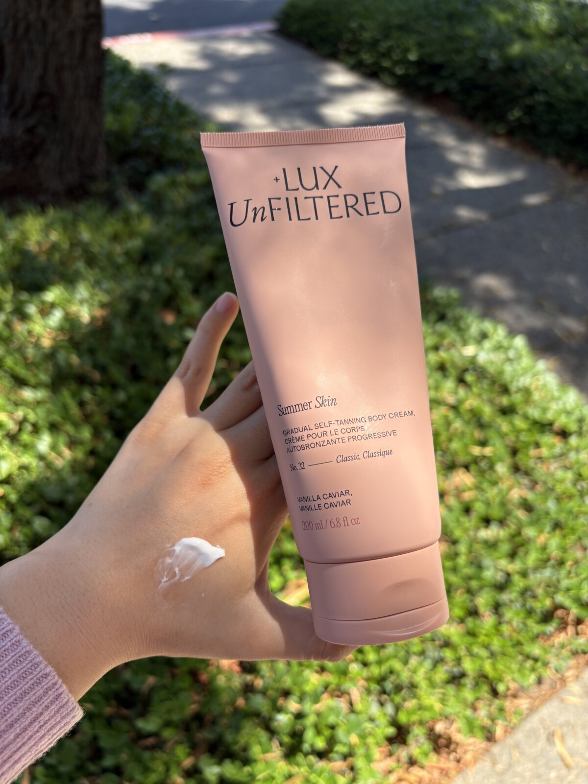 +Lux Unfiltered Body Cream, a luxury gradual tanning lotion. Shown in hand with a swatch.