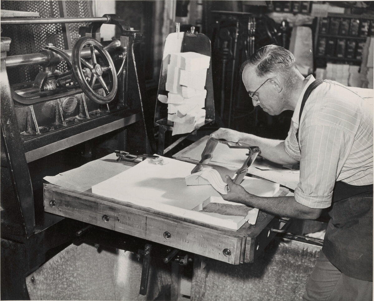 A worker for the paper-making company Crane cuts envelopes with a die (a metal tool for cutting materials). (Crane Museum of Papermaking and Center for the Paper Arts)