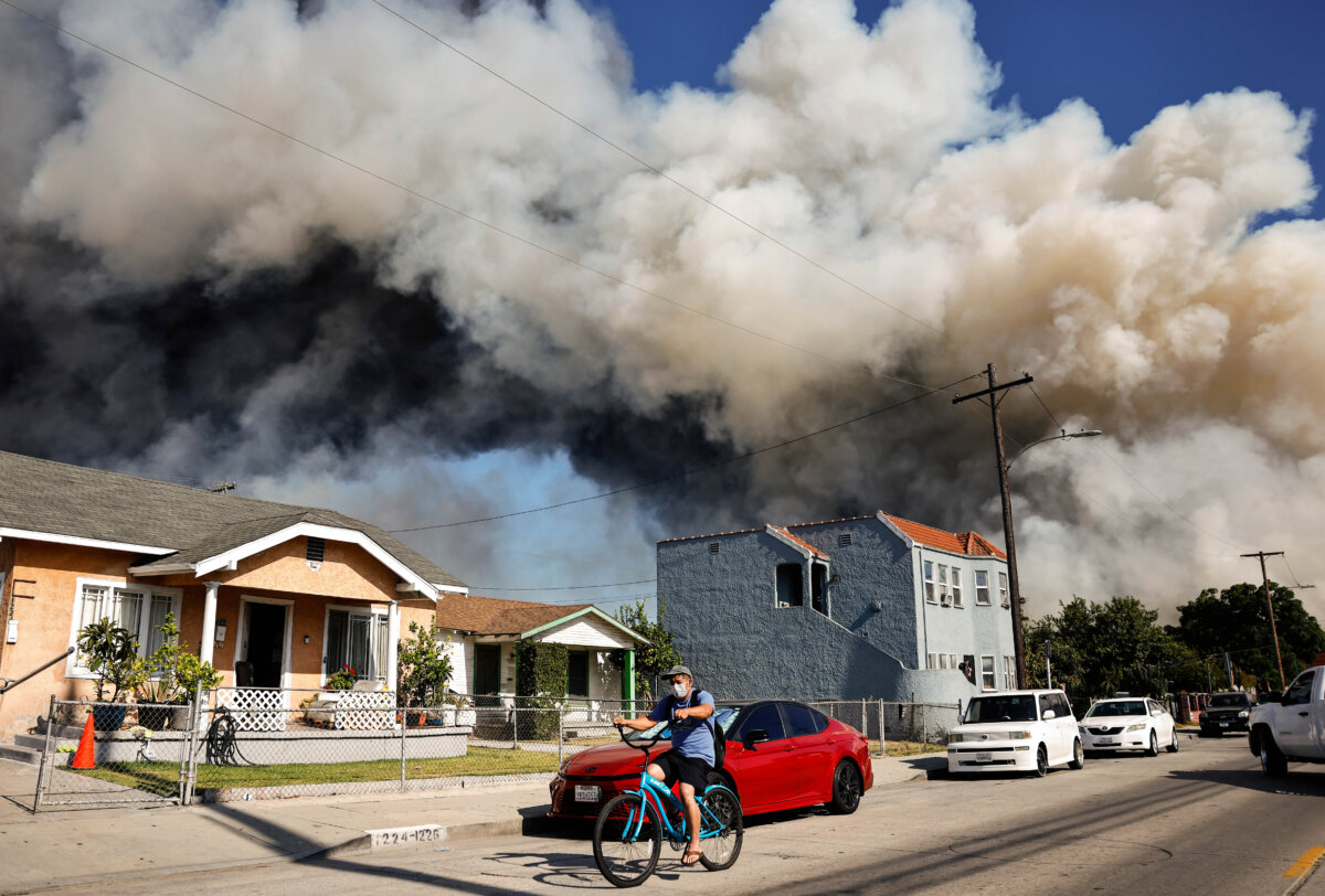 A man rides a bicycle as a massive warehouse fire in a cold storage facility continues to burn and spread smoke around Los Angeles on June 20, 2026. (Mario Tama/Getty Images)