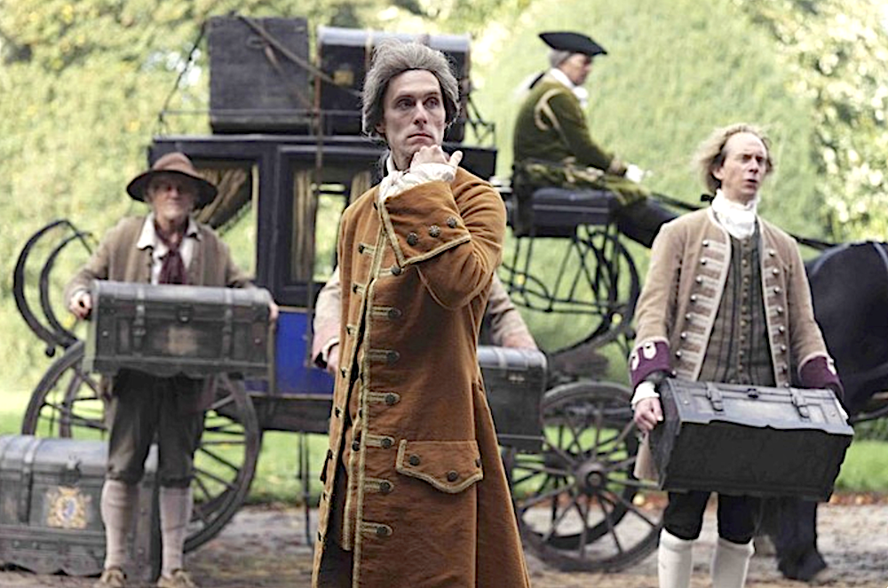 man in brown coat in front of stage coach in Savage House