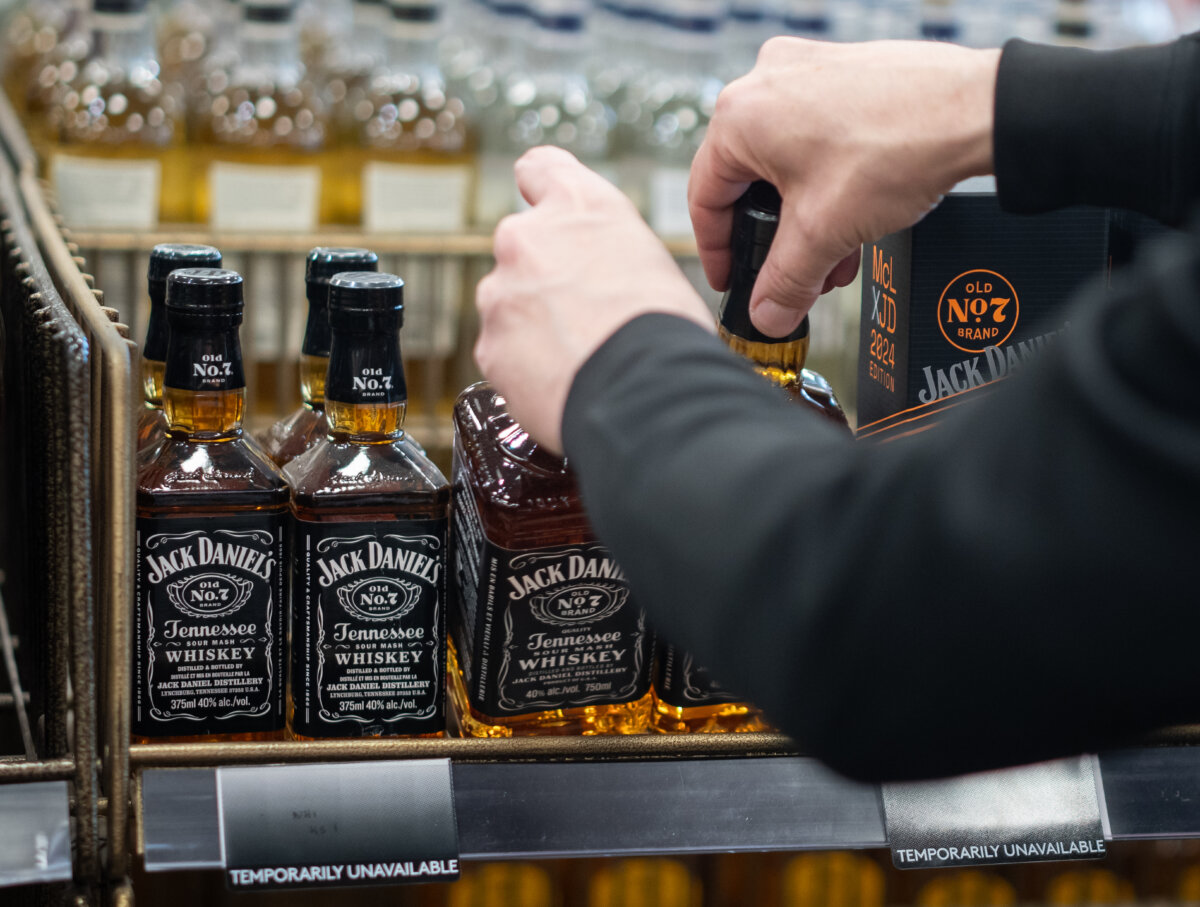 A B.C. Liquor Store employee demonstrates removing bottles of American whiskey for media before a news conference in Vancouver, B.C., on Feb. 2, 2025. (The Canadian Press/Ethan Cairns)