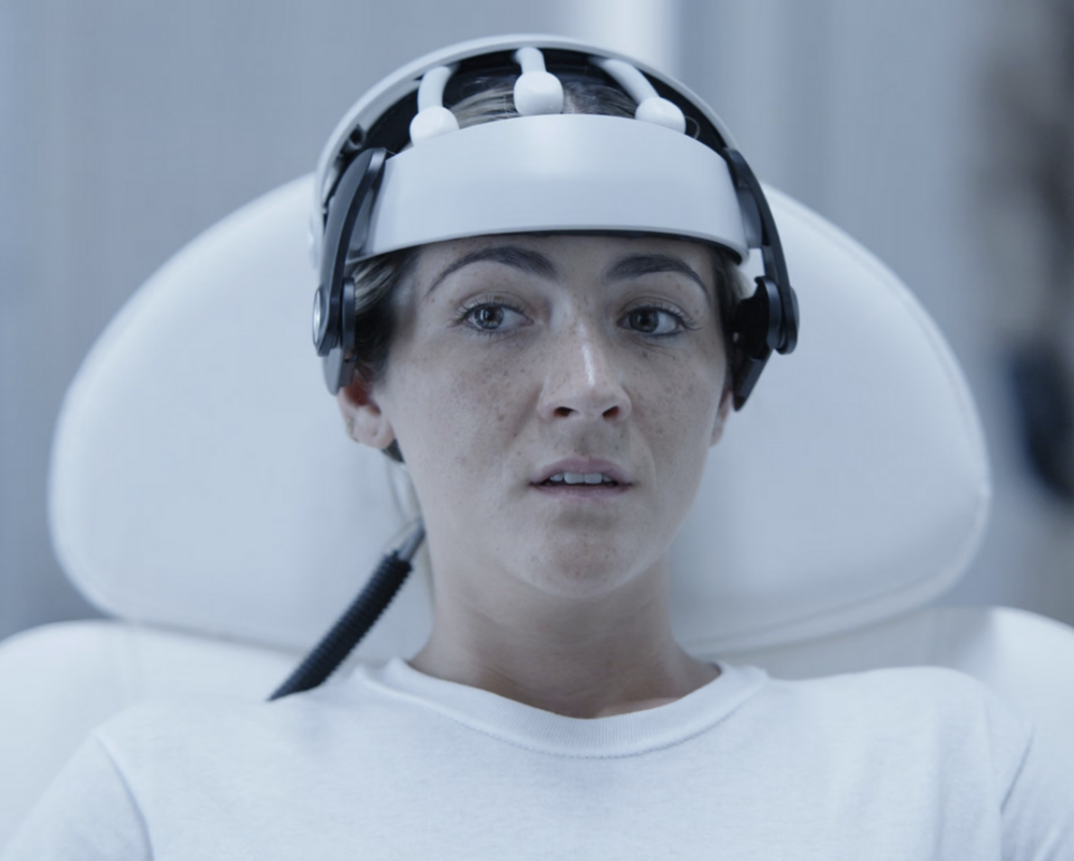 Woman in white chair wearing a brain activity scanner device in Signal One