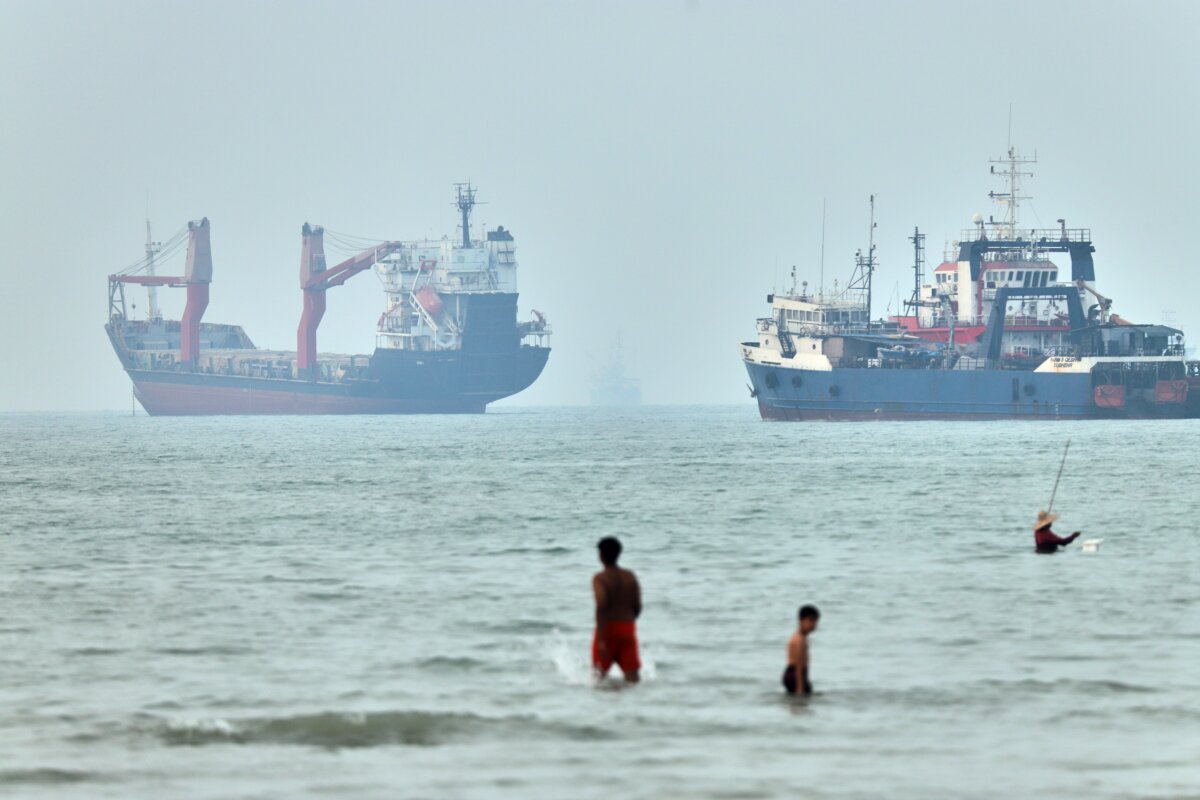 Children wade in the water with cargo ships at anchor in the background and a fisherman nearby, in the Strait of Hormuz off Bandar Abbas, Iran, on June 30, 2026. (Amirhosein Khorgooi/ISNA via AP)