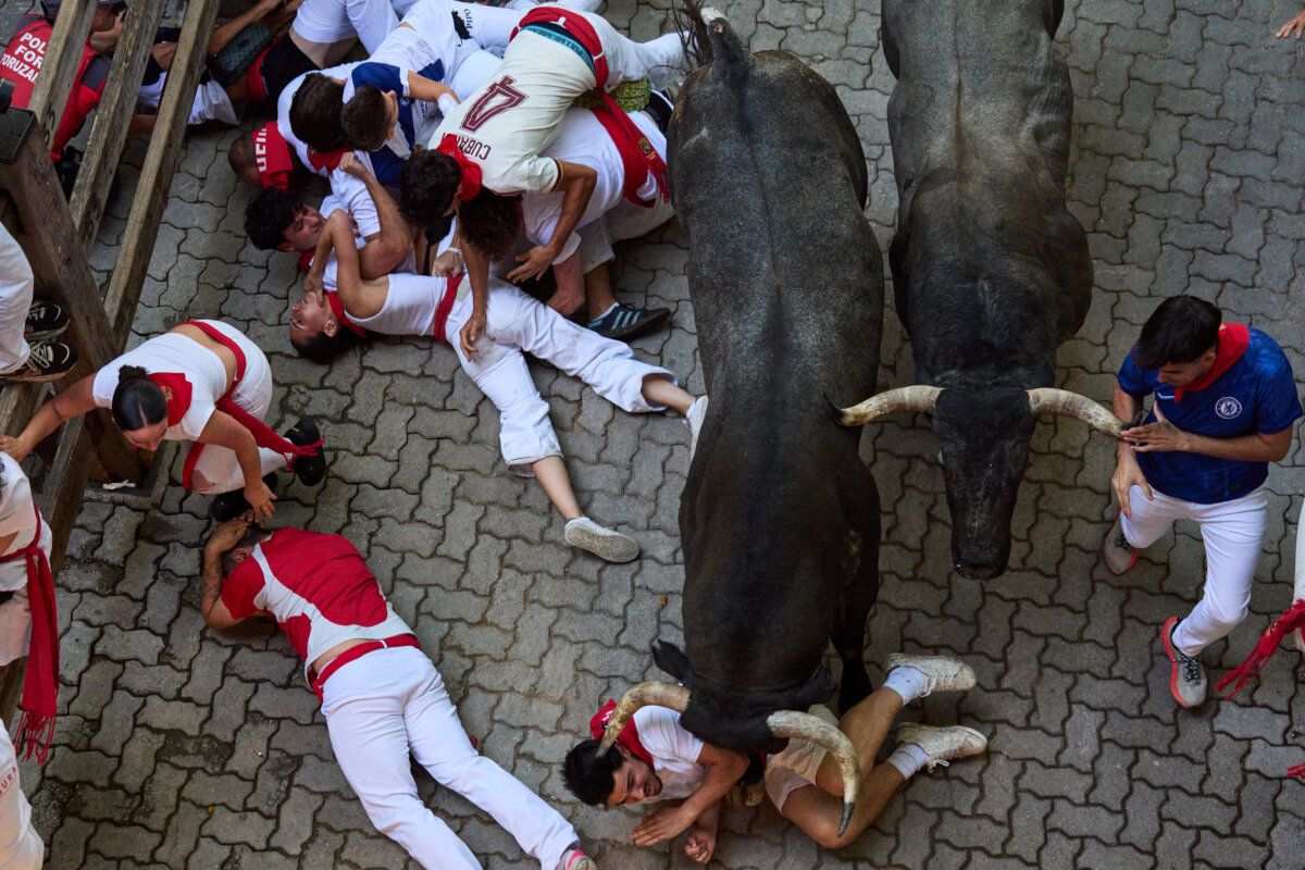 Revelers fall next to Jose Escolar's fighting bulls during the fifth running of the bulls at the San Fermín festival in Pamplona, Spain, Saturday, July 11, 2026. (Miguel Oses/AP Photo)