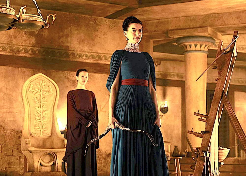 Women in blue holds a bow made from a ram's horn in The Odyssey