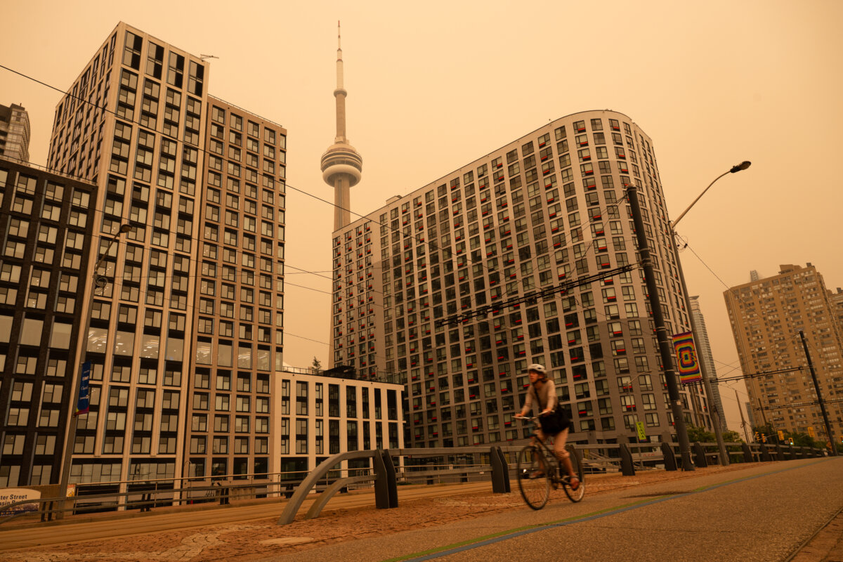 A woman bikes along the waterfront in Toronto as wildfire smoke fills the city, on July 15, 2026. (The Canadian Press/Laura Proctor)