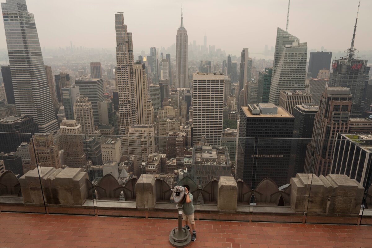 A person uses binoculars to look out as smoke from wildfires blankets the sky at Top of The Rock observation deck at the Rockefeller Center, July 16, 2026, in New York. (AP Photo/Yuki Iwamura)
