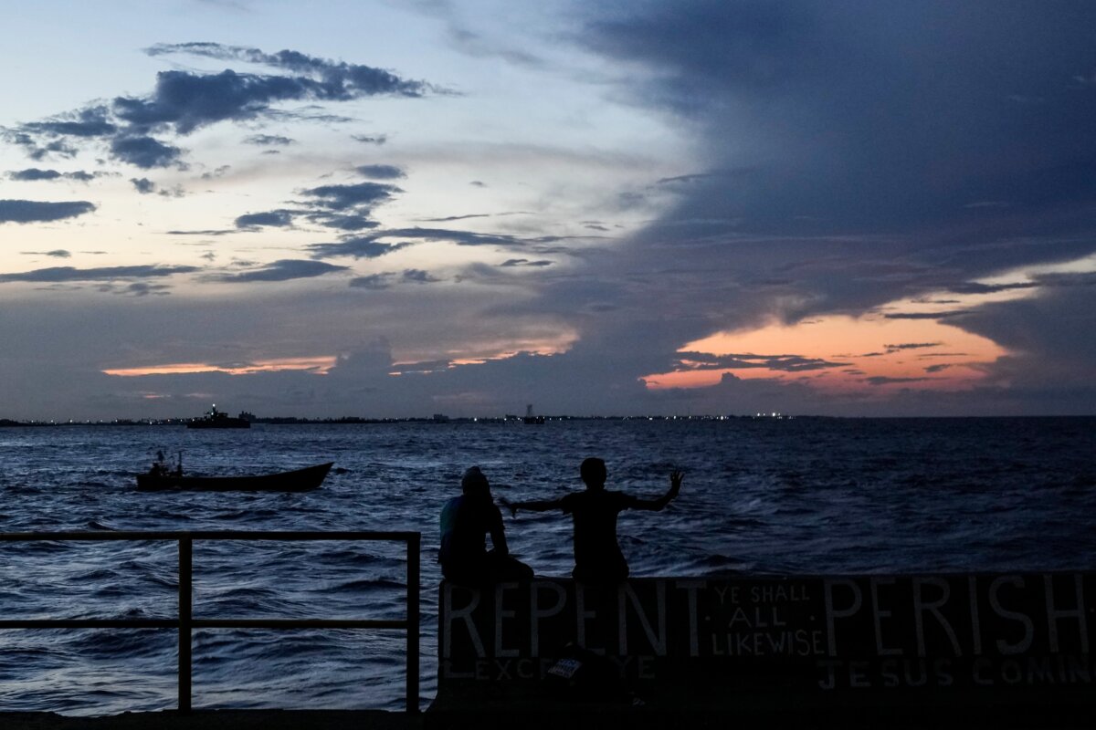 People sit on the seawall as the sun sets in Georgetown, Guyana, Tuesday, Nov. 19, 2024. (Matias Delacroix/AP Photo)