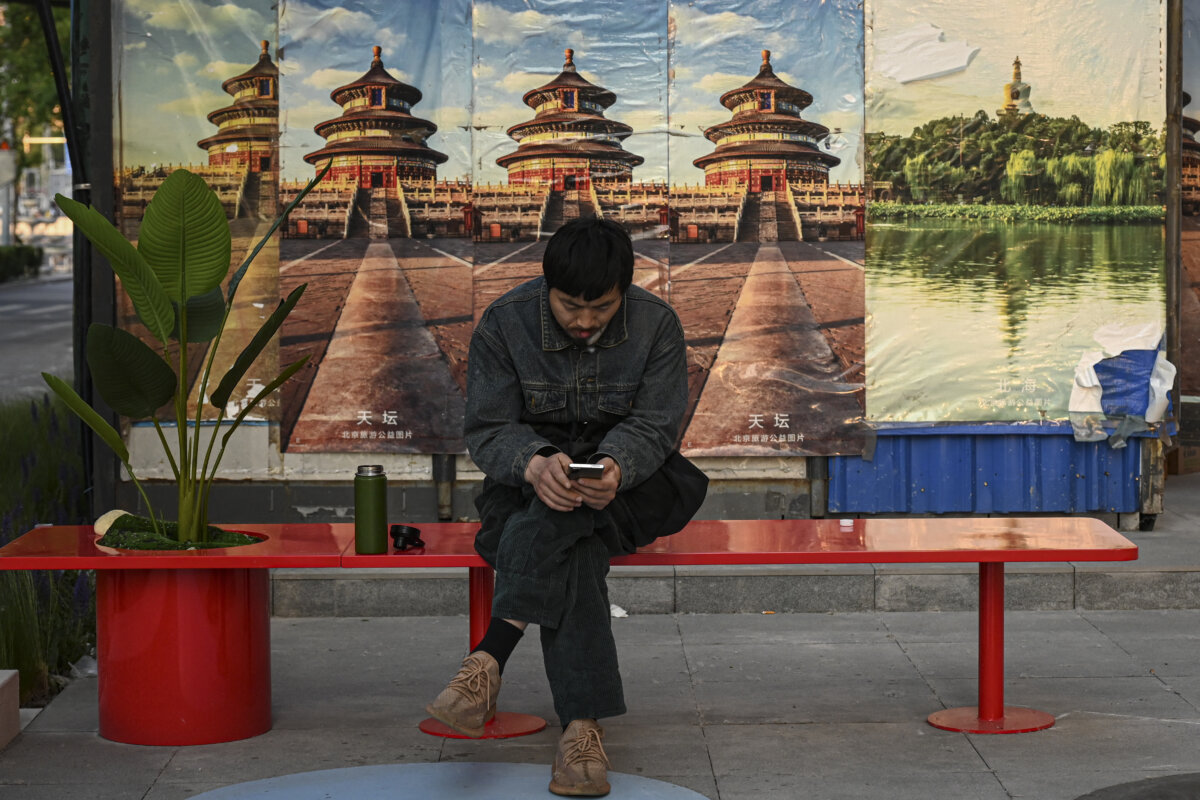 A man checks his mobile phone as he rests on a bench along a street in Beijing on May 6, 2025. (Jade Gao/AFP via Getty Images)