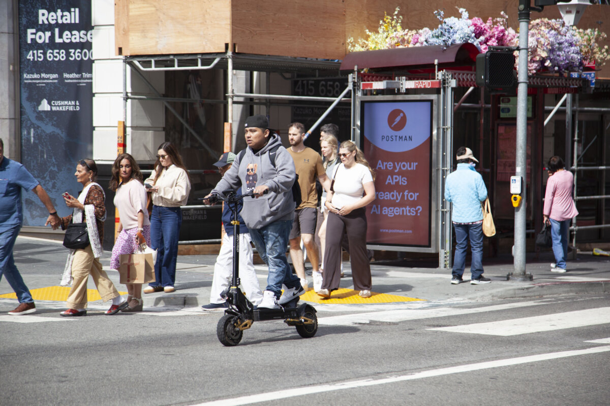 A man rides an e-scooter across an intersection near Union Square in San Francisco on Aug. 7, 2026. (Lear Zhou/The Epoch Times)