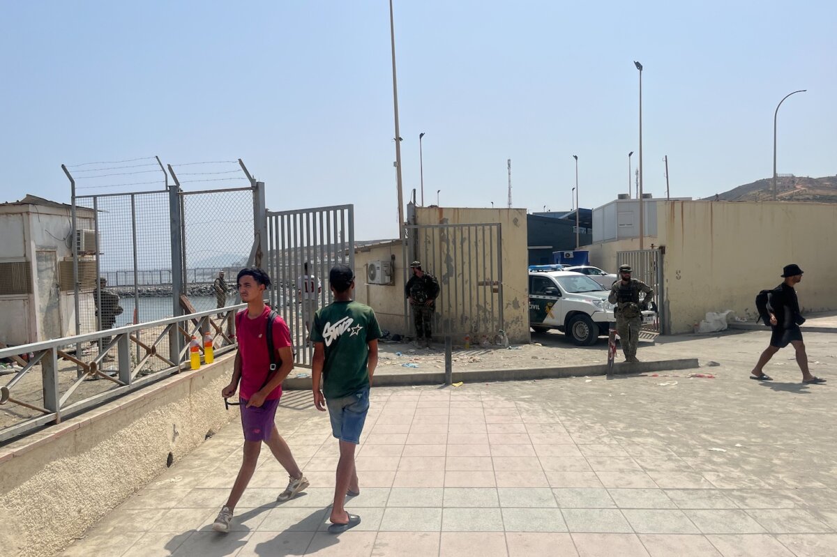 Moroccan migrants walk near the Spanish border with Morocco as Guardia Civil officers and military personnel stand alongside a Guardia Civil vehicle in Ceuta, Spain, on Aug. 1, 2026. (Etienne Fauchaire/The Epoch Times)