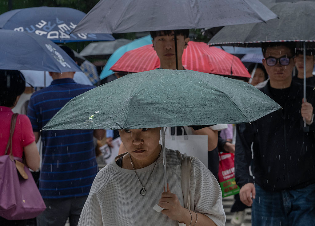 Commuters carry umbrellas as they walk in the street during a rainstorm caused by Typhoon Dolphin in Beijing on Aug. 12, 2026. (Kevin Frayer/Getty Images)