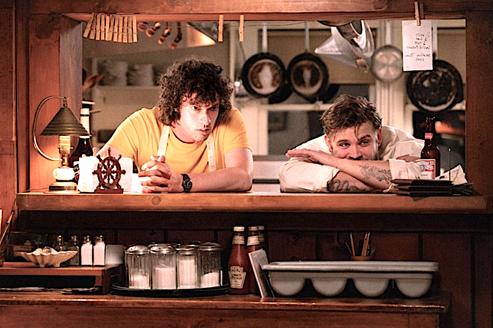 two young men lean on a restaurant kitchen counter in Tony