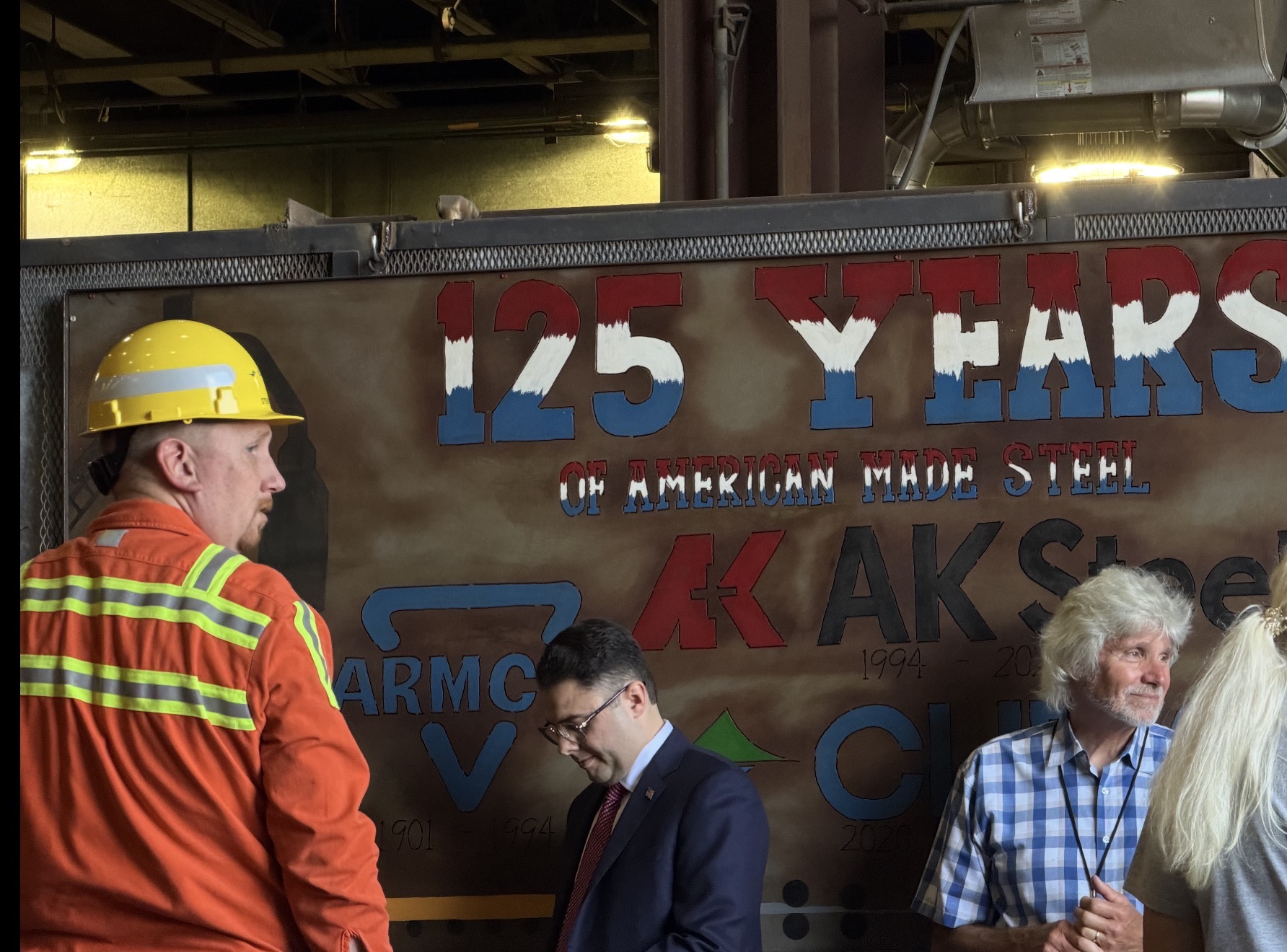 A steelworker stands in front of a poster
