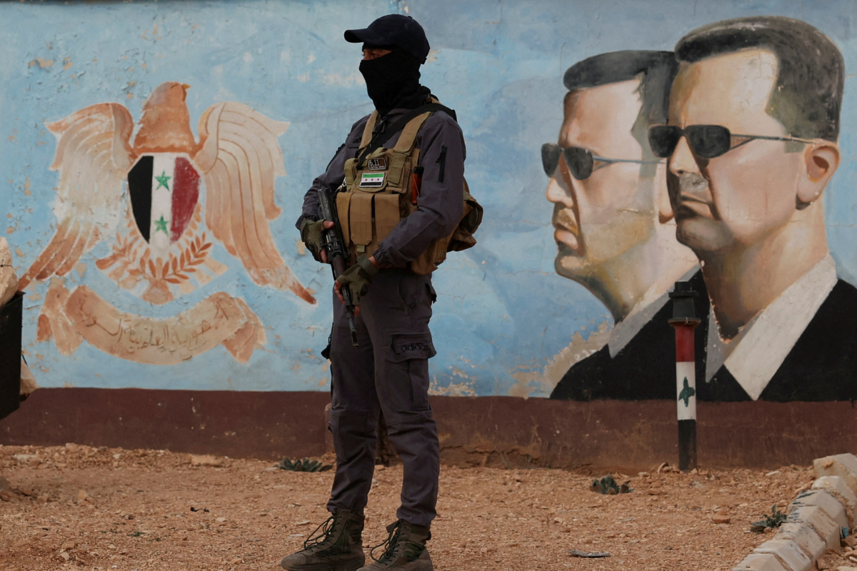 A member of former rebel group Hayat Tahrir al-Sham stands guard near an image of Syria's Bashar al-Assad at the fourth division headquarters in Damascus on Jan. 23, 2025. (Yamam Al Shaar/Reuters)