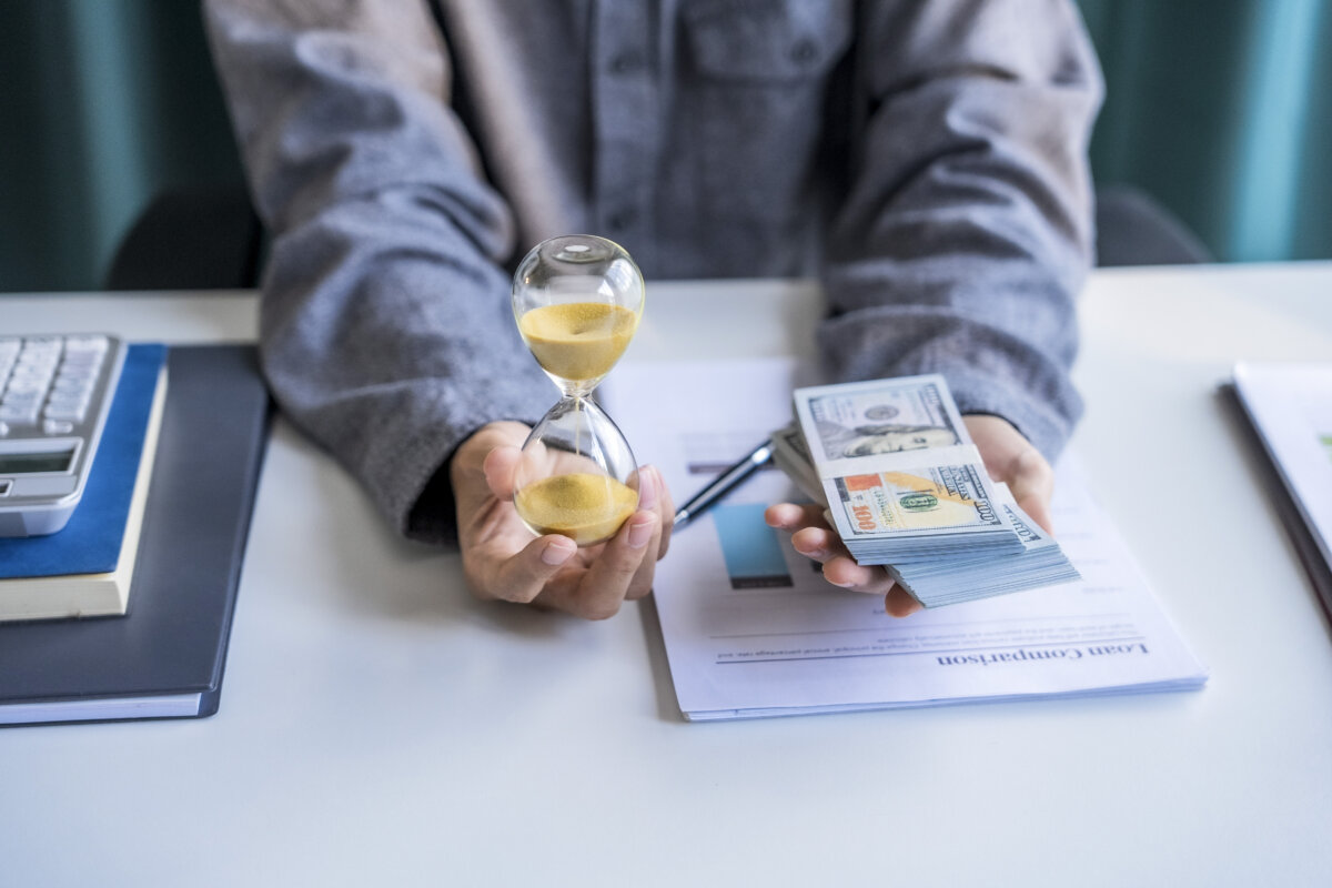 Asian businessman holding hourglass and cash in hands.