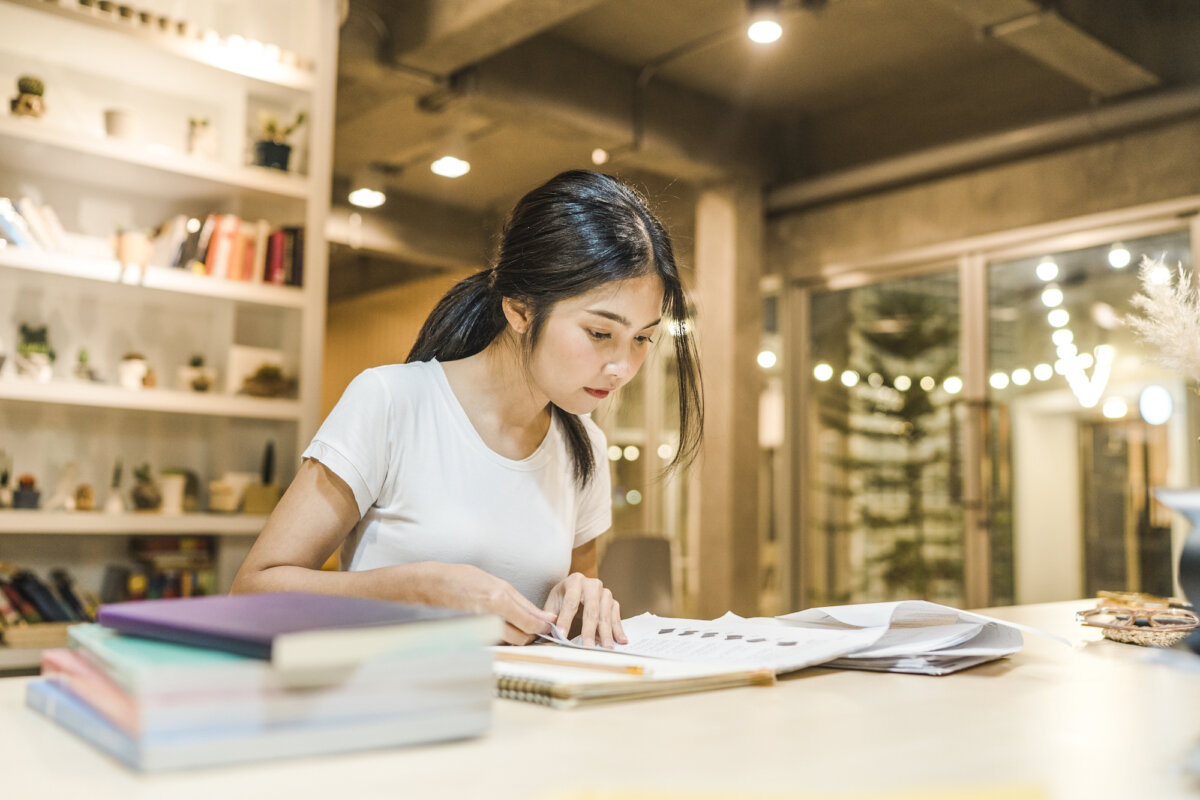 Asian student women reading books in library at university. Young undergraduate girl do homework, read textbook, study hard for knowledge on lecture desk at college campus overtime night.