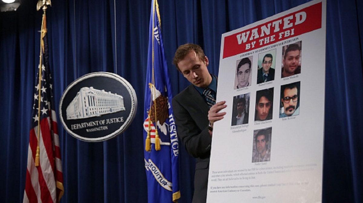 A Department of Justice employee put up a poster of the seven indicted hackers prior to a news conference