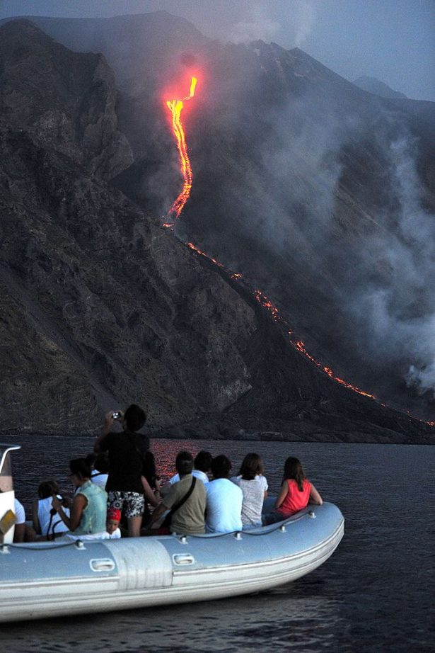 A boat of tourists watches as lava from the Stromboli volcano