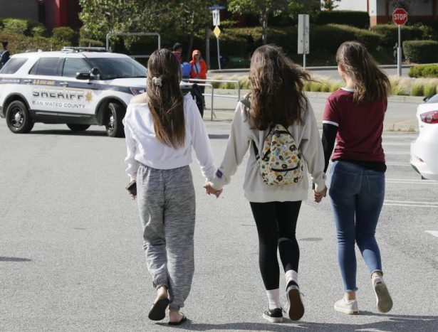 Three teens hold hands after being escorted