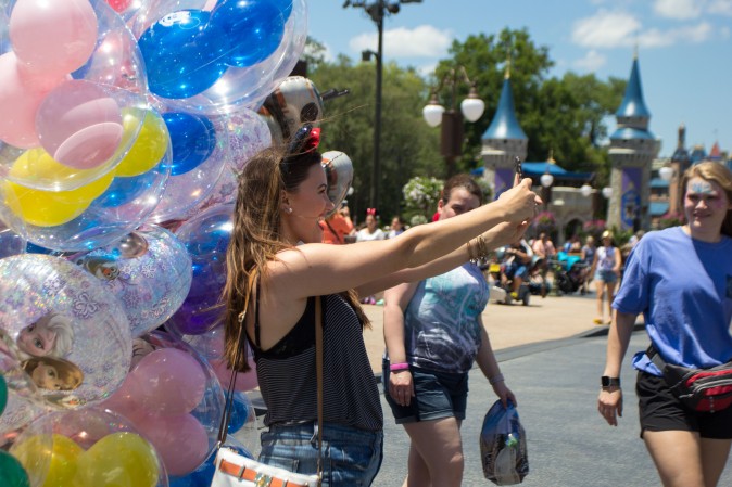 A woman takes a selfie with Mickey Mouse shaped balloons at the Magic Kingdom park in Orlando on May 22, 2016. (Benjamin Chasteen/Epoch Times)